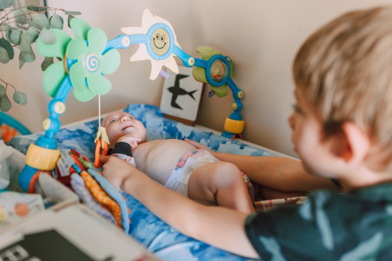 our-story A cute baby lying in a crib, engaged with colorful hanging toys, depicting joyful childhood moments.
